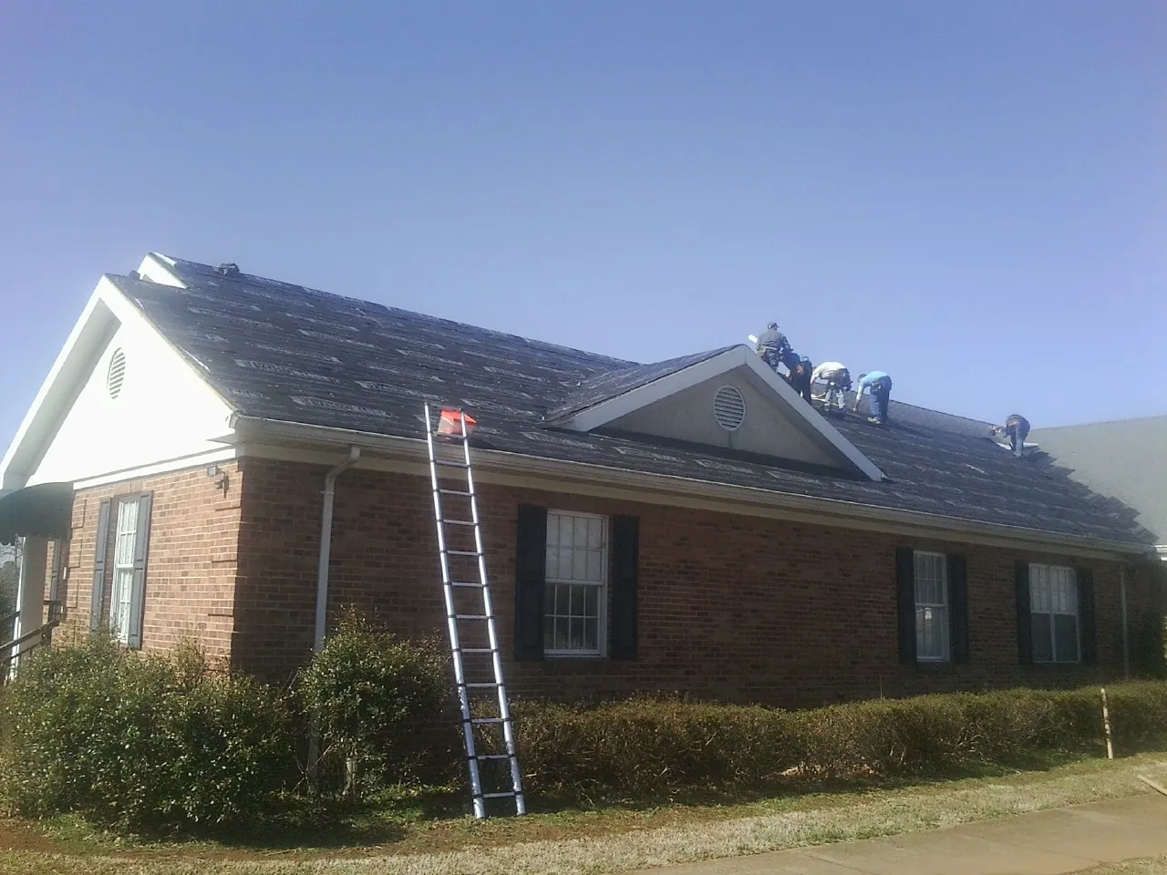 Crew tearing shingles off a brick ranch roof with a ladder set — Metal Roof Repair work by our crew in Sherrodsville