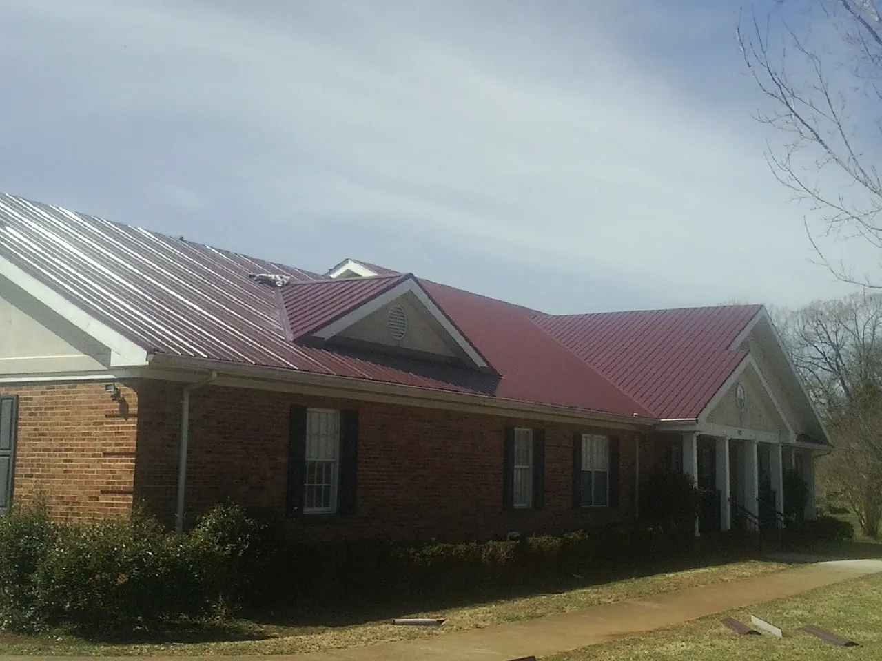 Red metal roof with gabled entries on a long brick building, from a Hail Damage Roof Repair job in Sherrodsville
