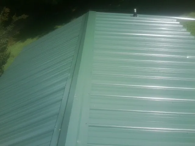 New green metal panels meeting at the ridge of a roof — Flat Roof Repair work by our crew in Sherrodsville