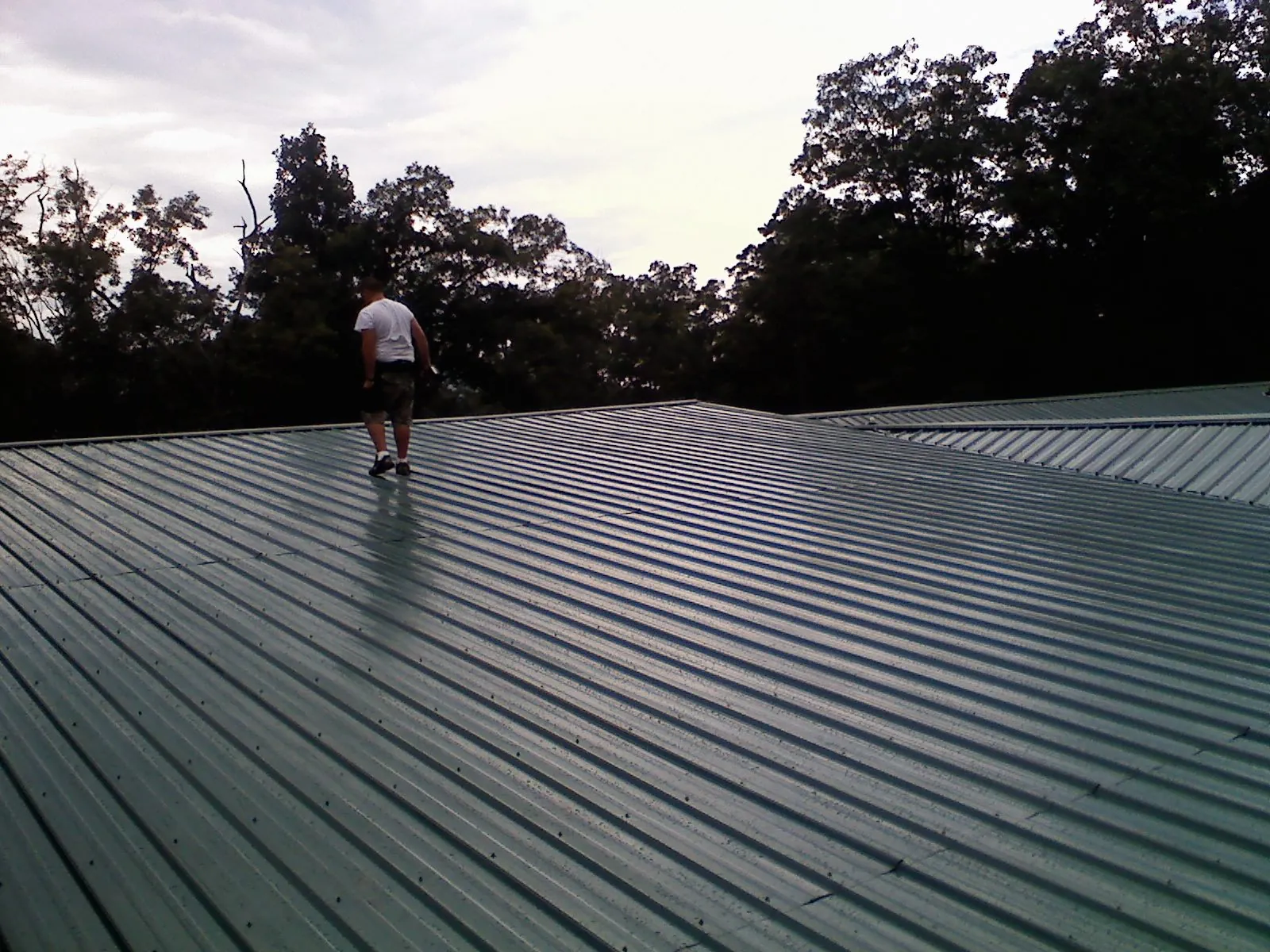 Roofer walking a wide expanse of new green metal roofing in Sherrodsville