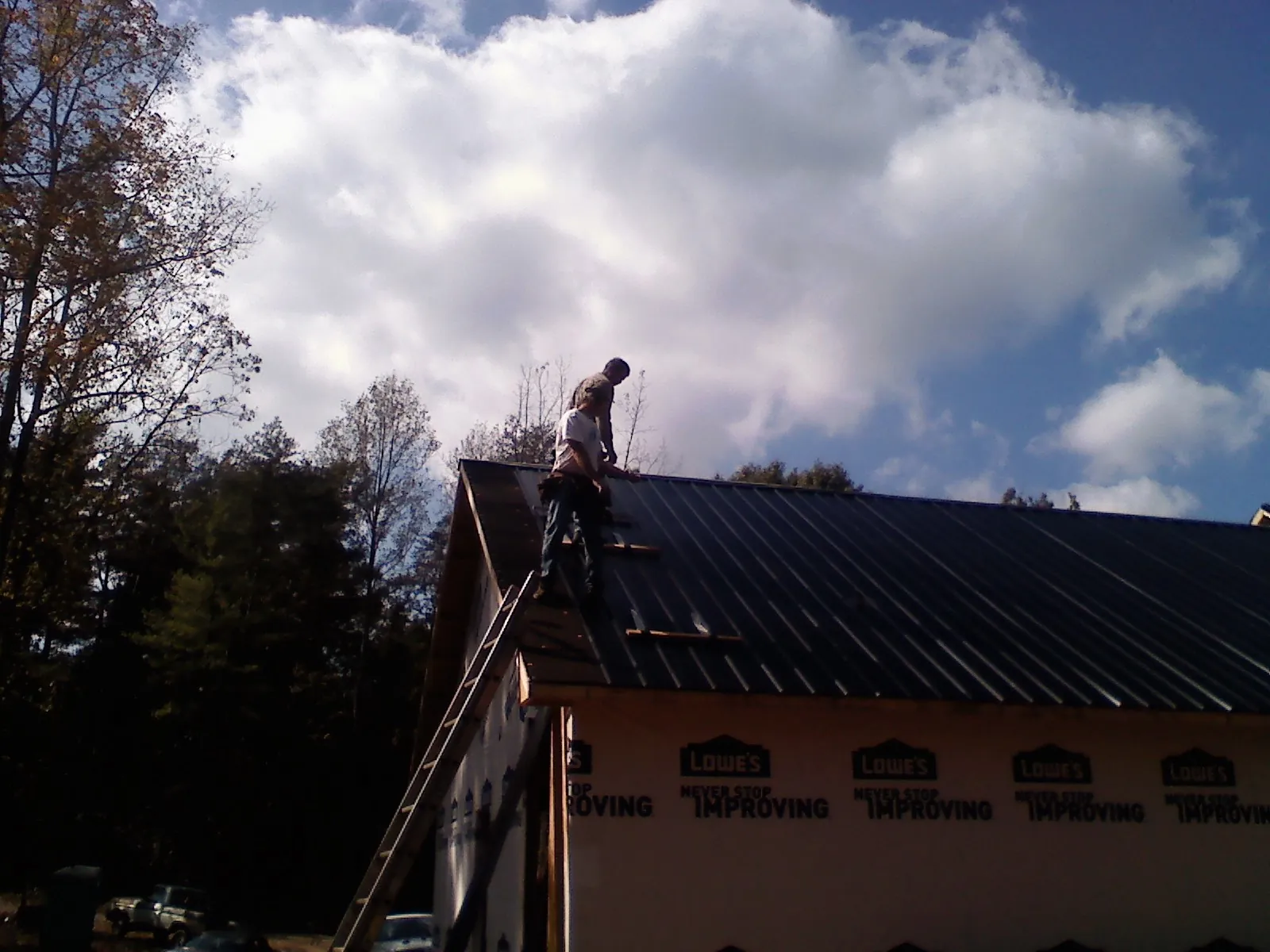 Roofer fastening dark metal panels high against a cloudy sky, from a Roof Inspection job in Sherrodsville