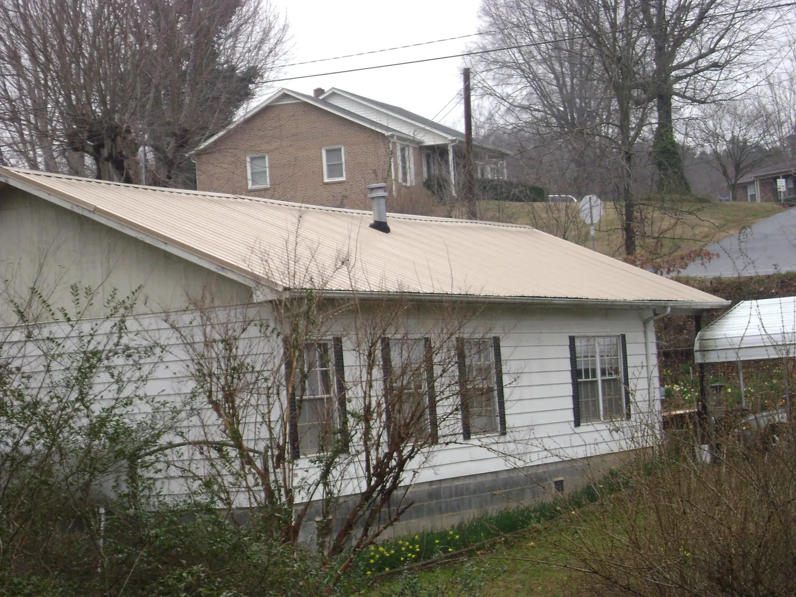 Tan metal roof on a white sided house set into a hillside — Commercial Roofing by Roofing Brothers in Sherrodsville